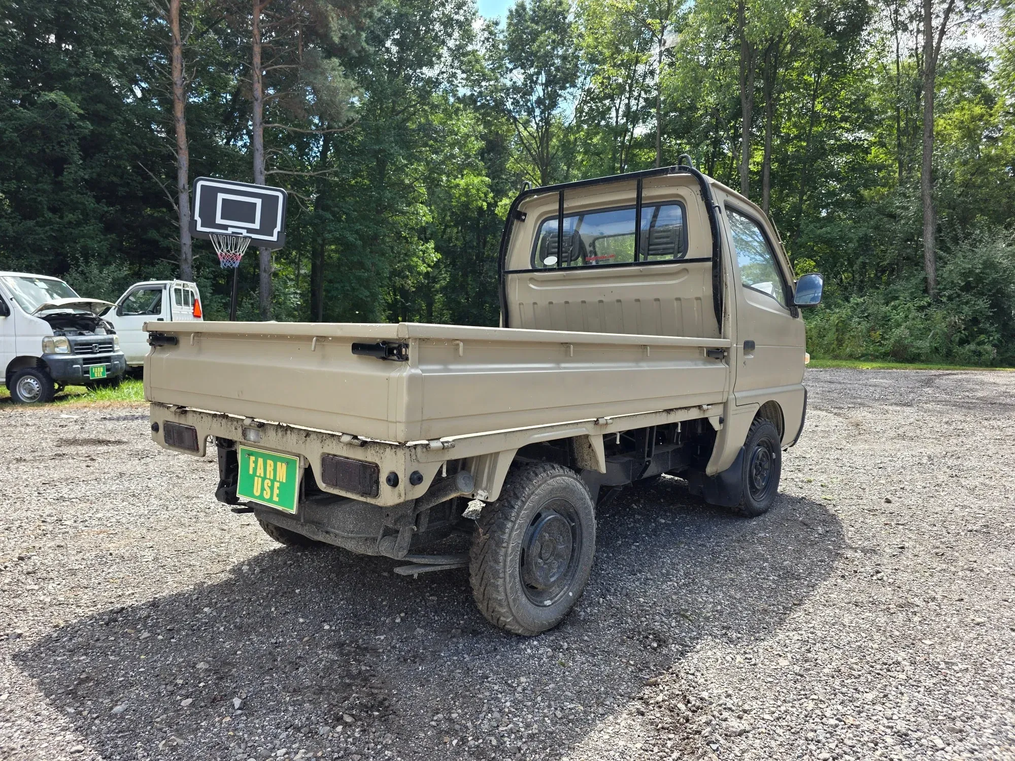 Tan flatbed Japanese mini truck marked for farm use, rear view